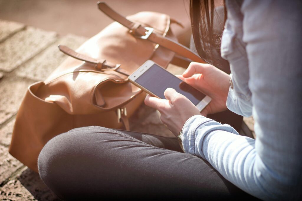 pexels-photo-359757-359757 Woman sitting with smartphone and brown bag in sunlight.